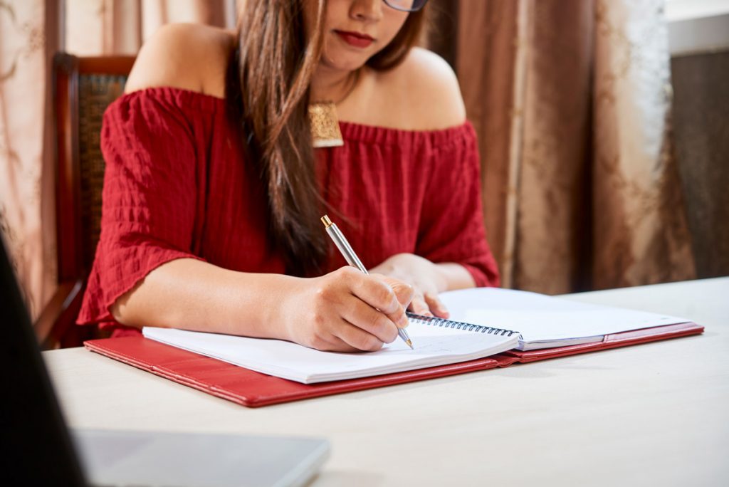 Female college student writing in textbook when working on project at home.