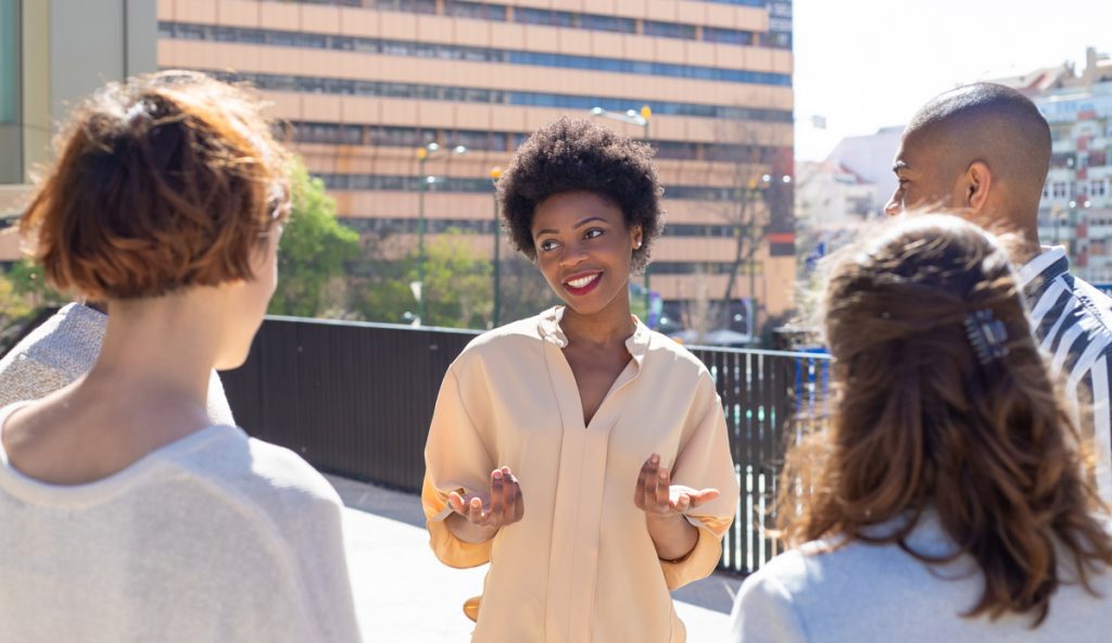 Group of young people standing on street and communicating. Smiling African American woman talking to friends.