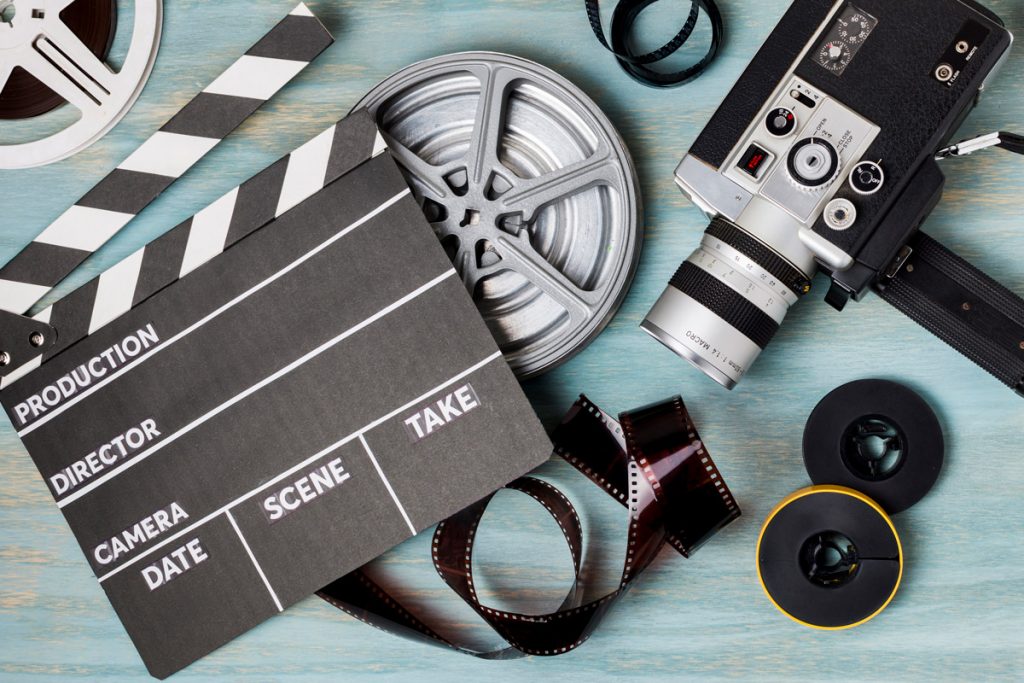 An elevated view of clapperboard; film reels; film strips and camcorder on blue wooden backdrop.