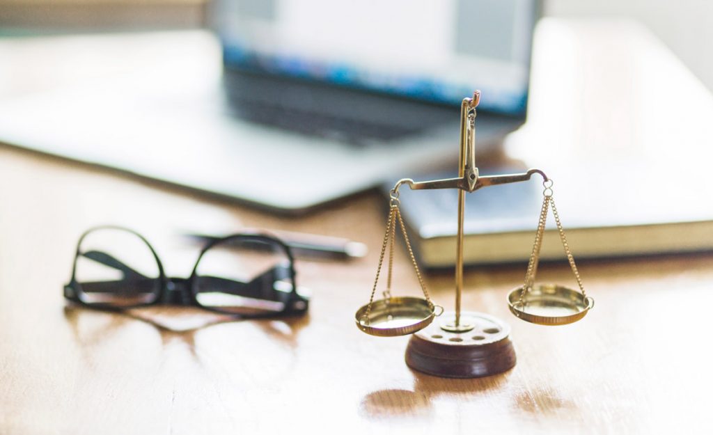 Justice scale and spectacles on wooden desk in courtroom.