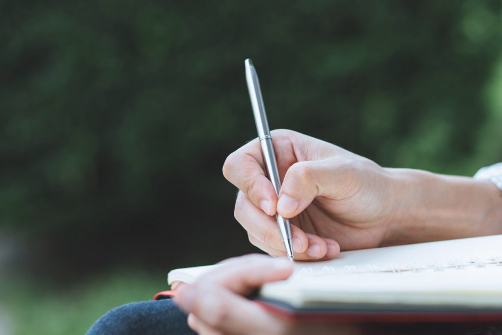 Close up hand young man are sitting using pen writing record lecture notepad into the book in the parks.