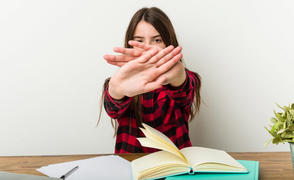 Young teenager going back to her routine doing homeworks doing a denial gesture.